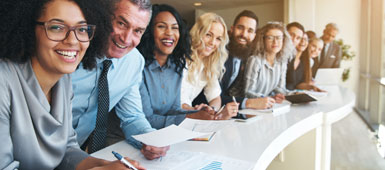 A diverse group of coworkers lean forward and smile at the viewer